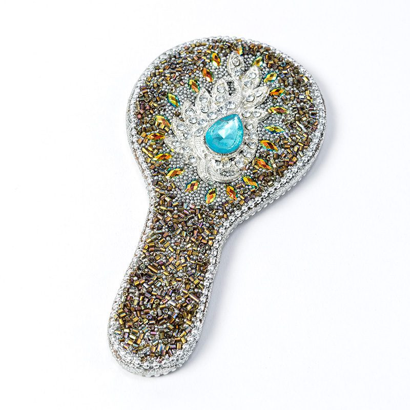 Our exquisite hand-held mirror adorned with peacock-coloured beads is the epitome of timeless beauty.